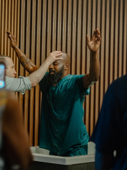 A man being baptized at Greater Faith, arms lifted